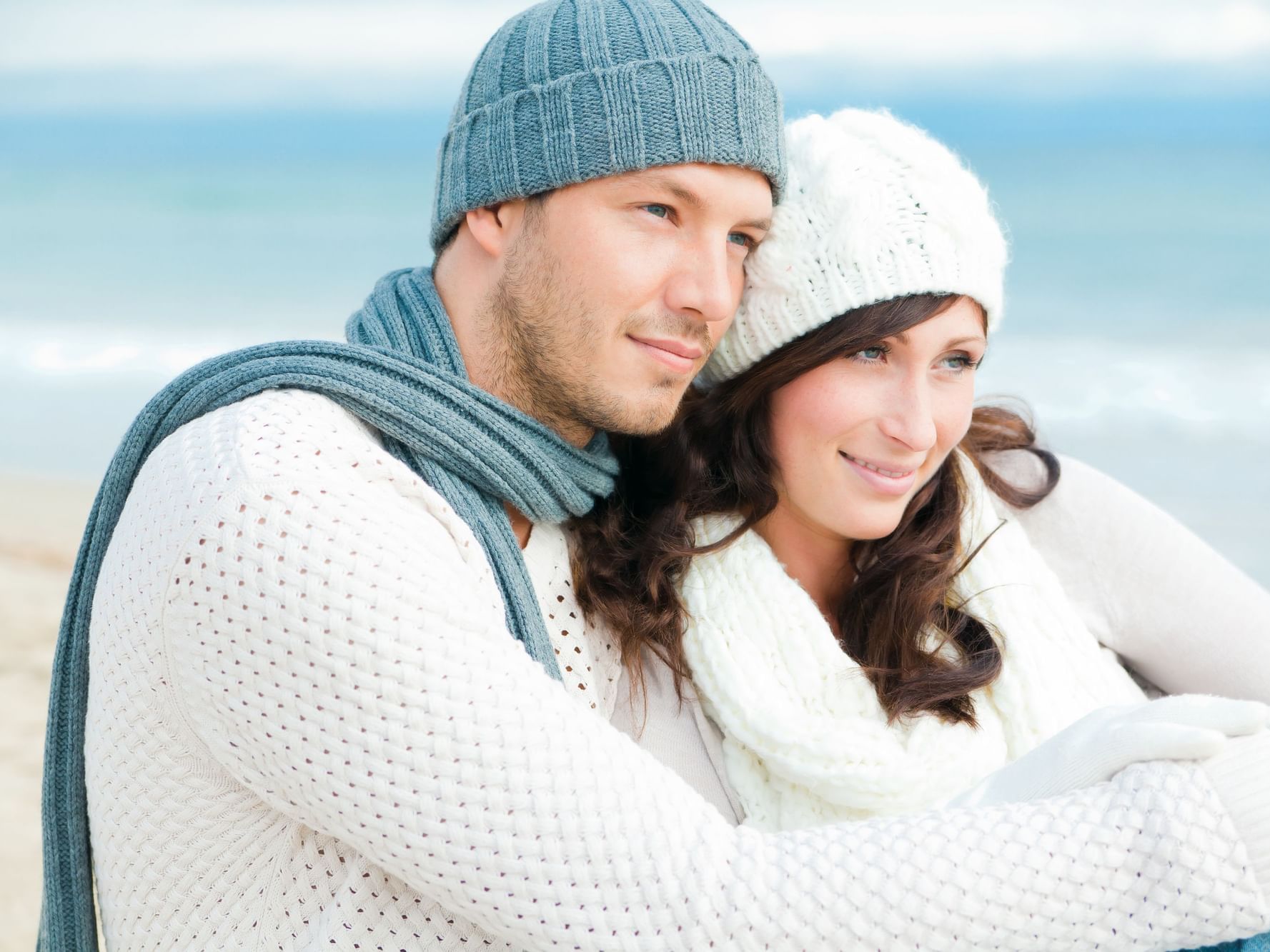 Couple embracing on a beach near Ana Hotels Europa Eforie Nord, dressed warmly, with ocean waves gently rolling