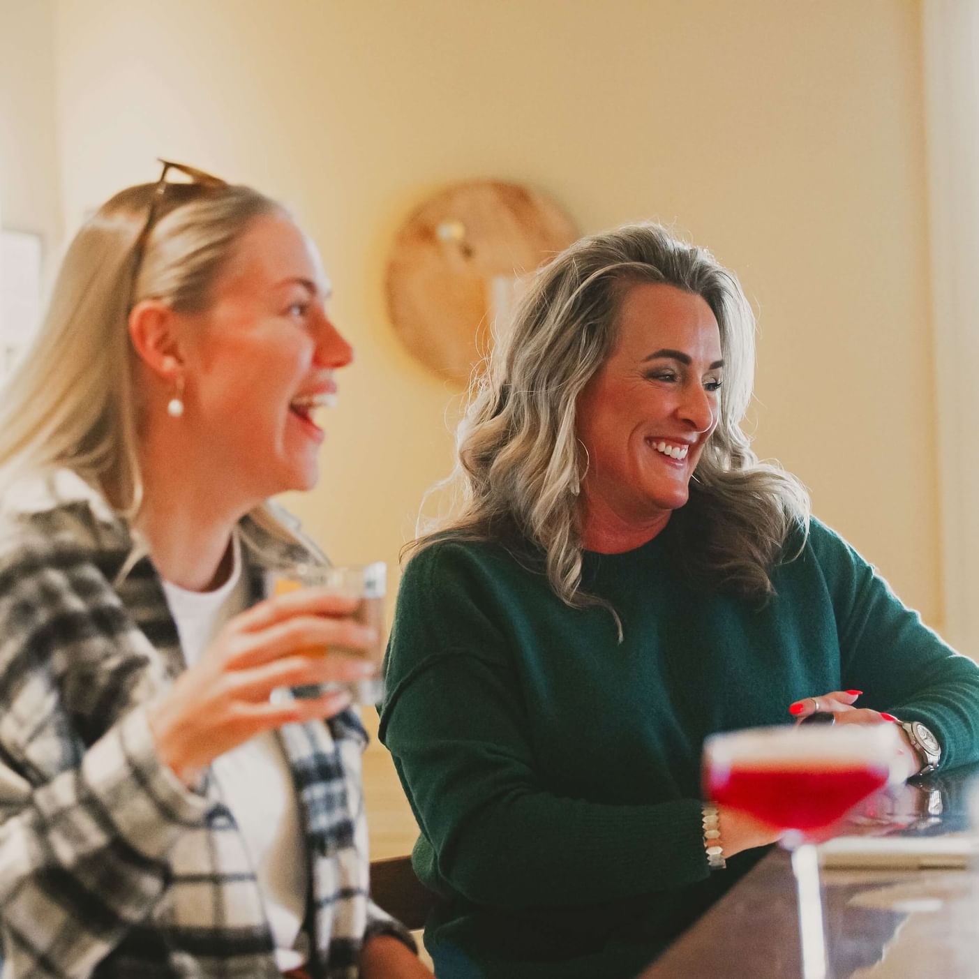 Two women laughing and holding drinks during Herb & Harvest- Garden Inspired Cocktail Workshop.