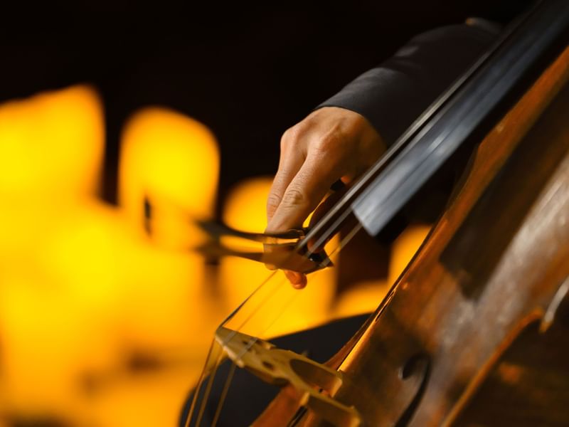 Close-up of a musician's hand playing a cello with warm golden lighting in the background for La Fête de la Musique