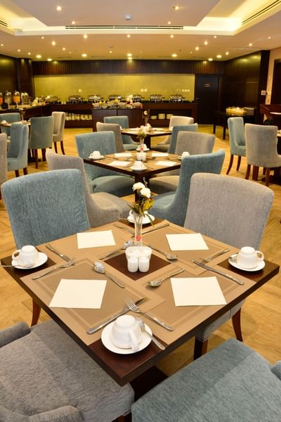 Square dining tables with white cups by plush blue chairs in Naviti Restaurant at Naviti By Warwick Dammam