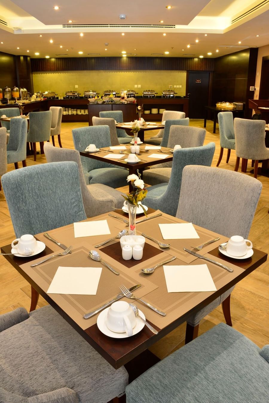 Square dining tables with white cups by plush blue chairs at Naviti By Warwick Dammam