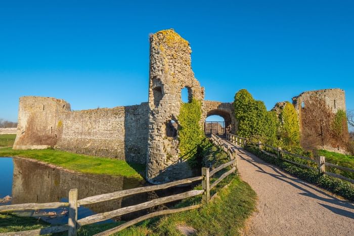 Ancient stone ruins with a wooden fence and path leading to a gateway under a clear blue sky.