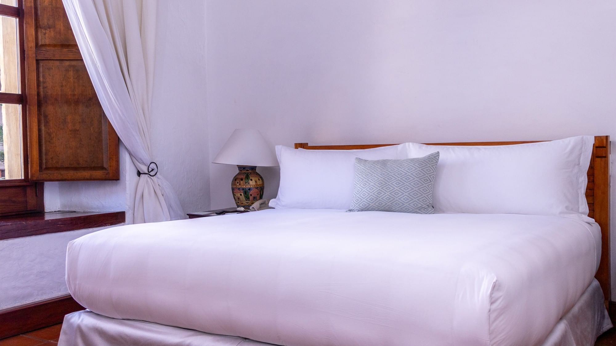 Cama blanca de hotel con lámpara decorativa y contraventanas de madera en Quinta Real Oaxaca