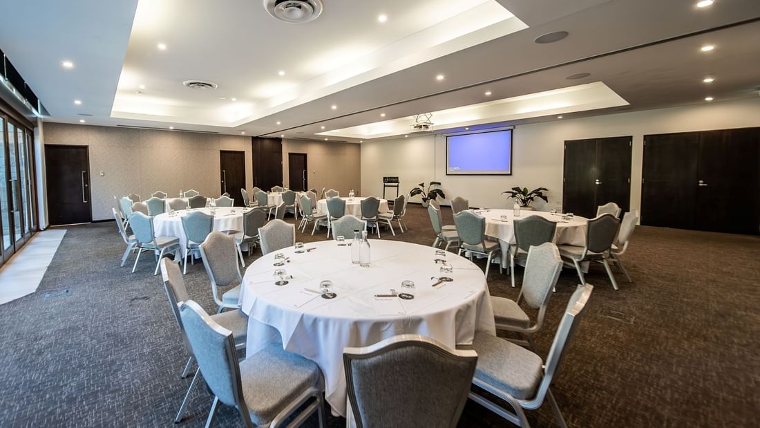 Temple Room with round tables, chairs & projector screen on the wall at Pullman Port Douglas