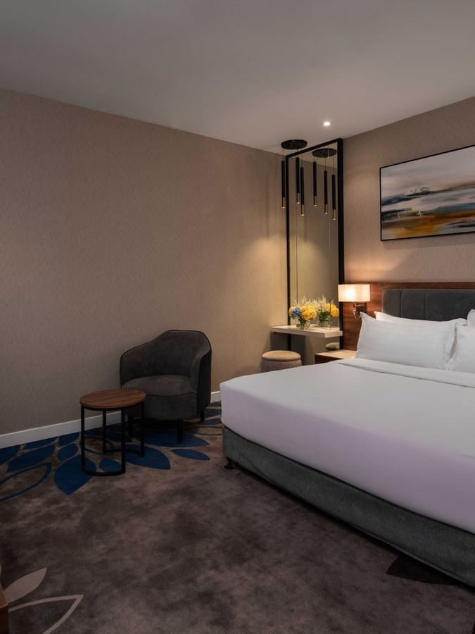 Standard Room with a king bed by a small round table and armchair on a blue, floral patterned rug at Warwick Al Jubail