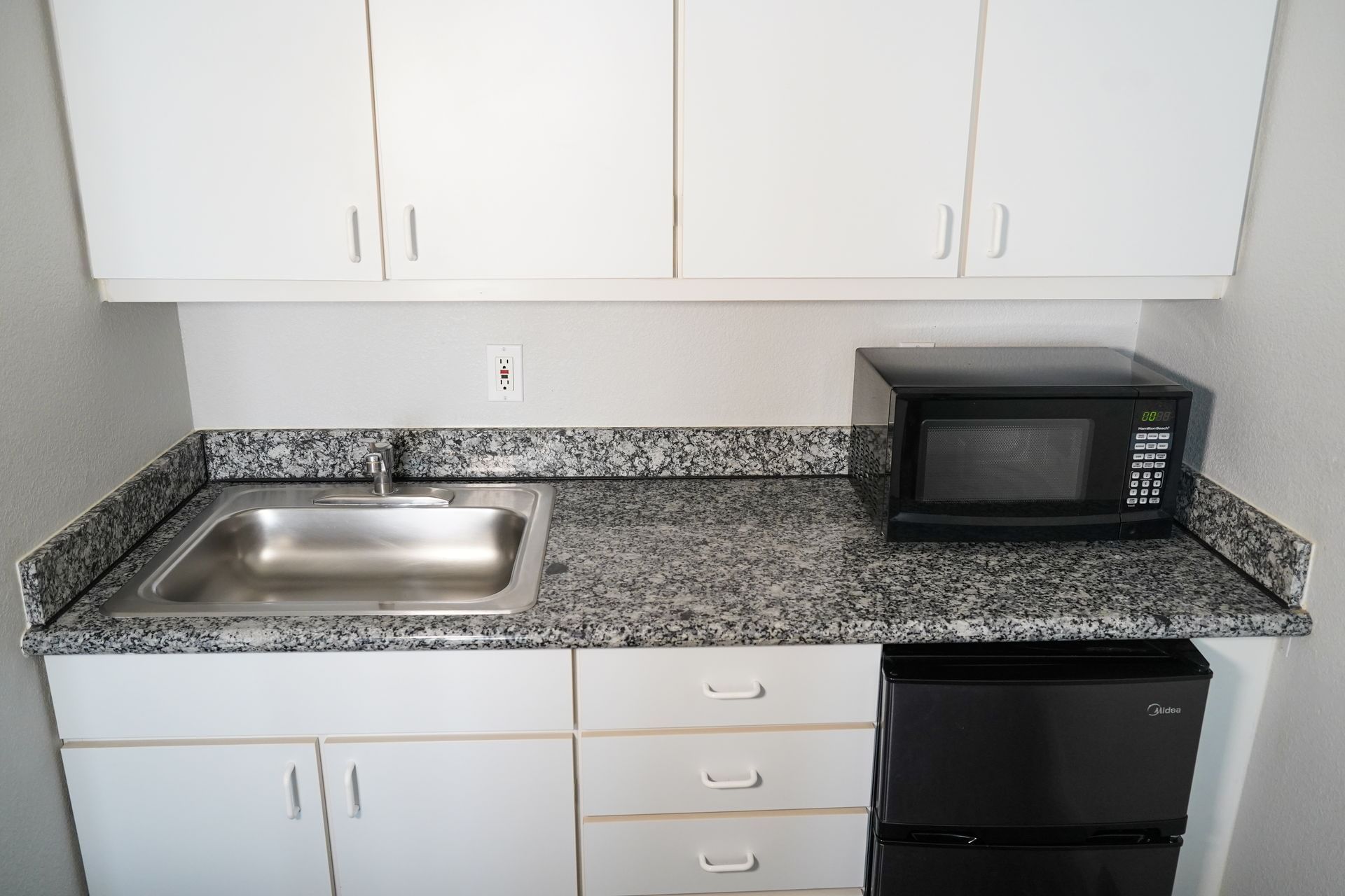 A compact kitchenette with a microwave, sink, and mini fridge.