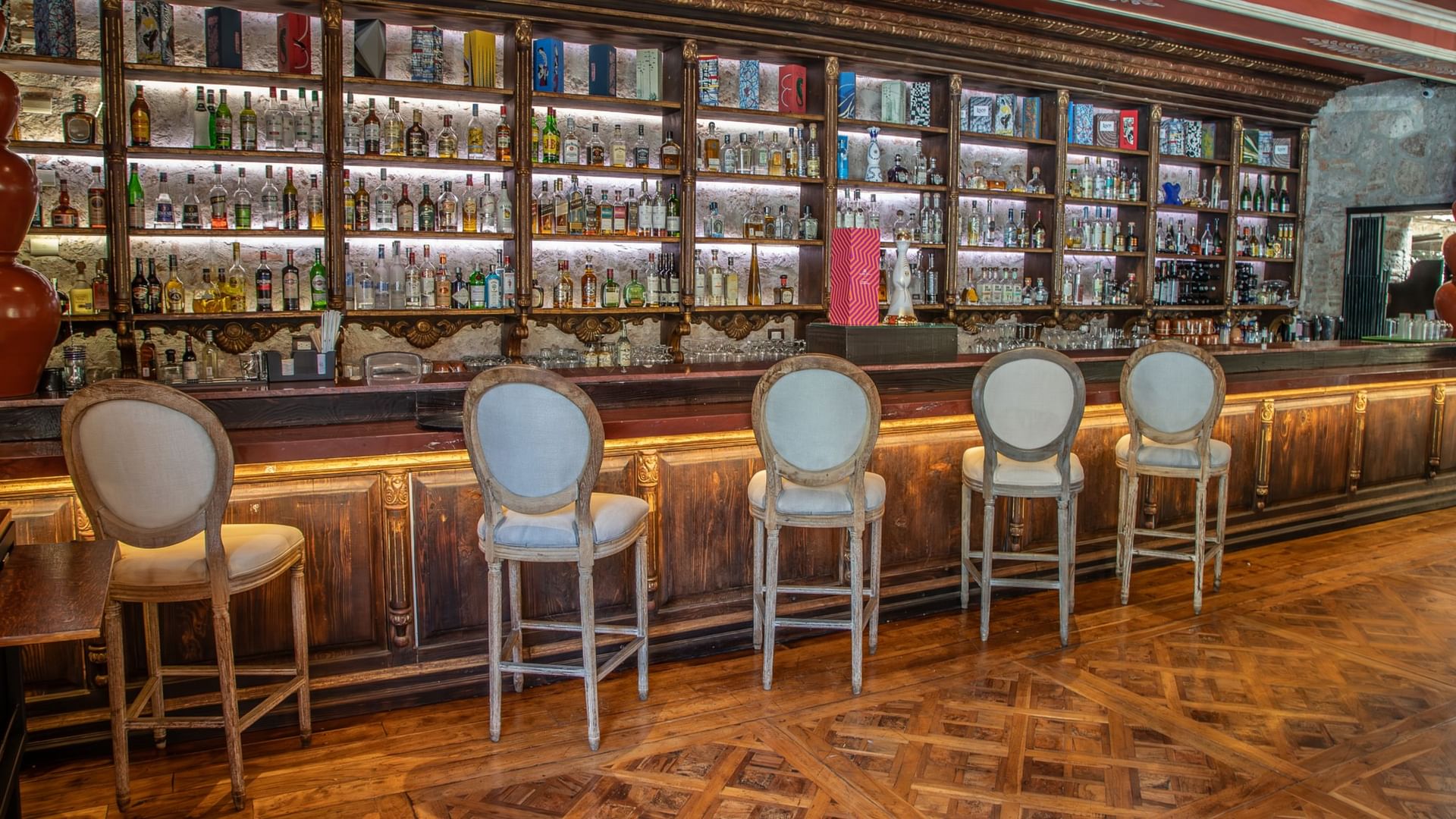 Elegant bar with upholstered stools, illuminated wood paneling, and backlit shelves displaying spirits at Quinta Real Guadalajara