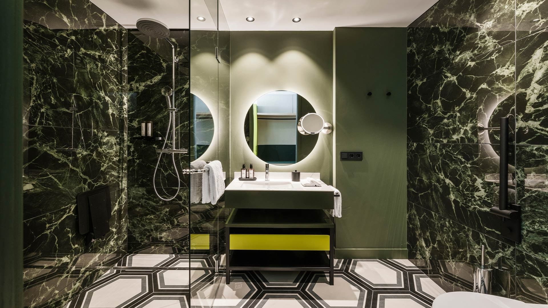 Modern bathroom with green marble walls and hexagonal floor at Falkensteiner Hotel Bozen WaltherPark in Bolzano.