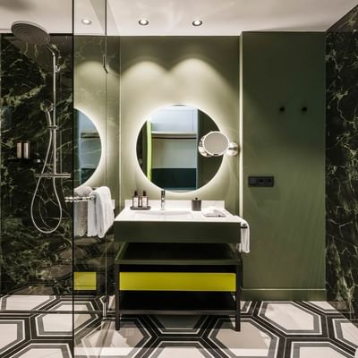 Bagno lussuoso con pareti in marmo verde e pavimento a mosaico al Falkensteiner Hotel Bozen WaltherPark, Bolzano.