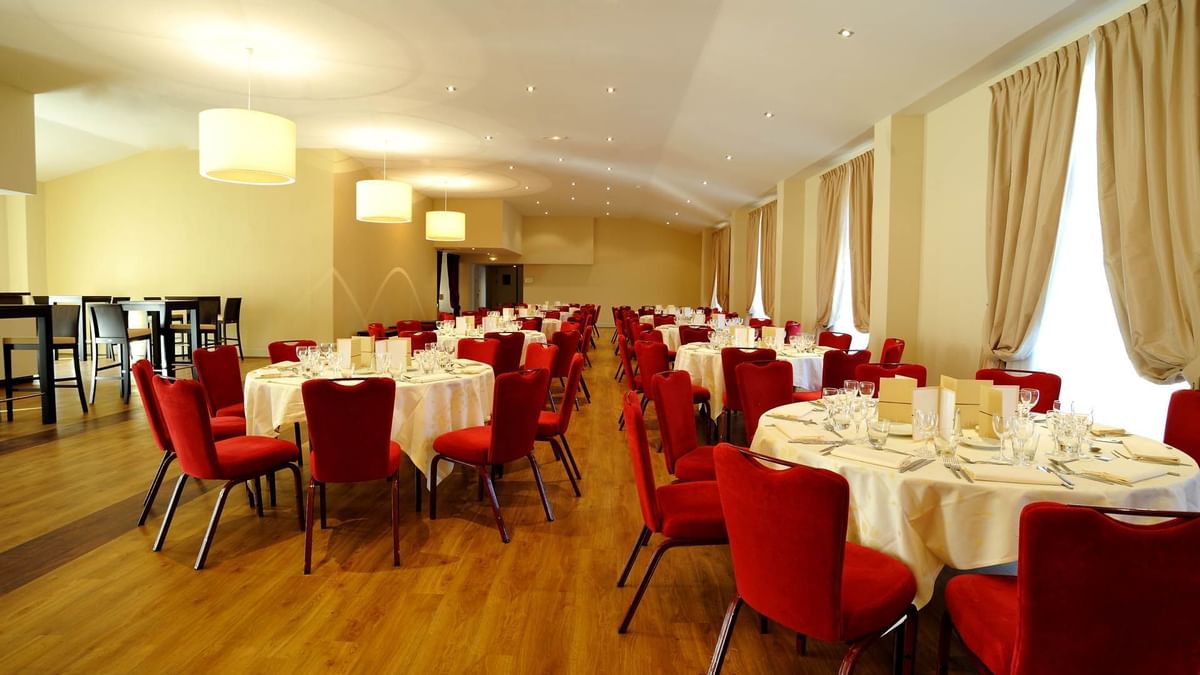 Une salle à manger élégante avec des tables rondes couvertes de nappes blanches et des chaises rouges.