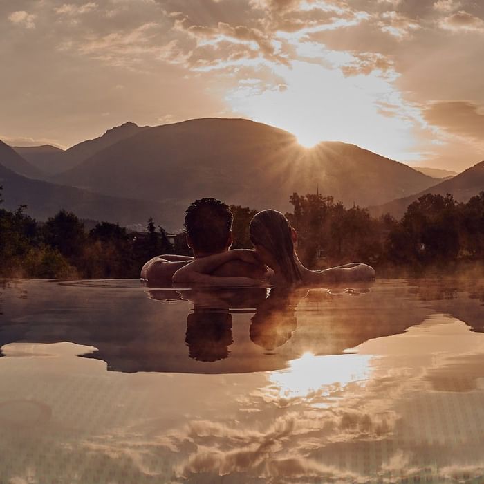 Coppia rilassante in piscina all'aperto al tramonto con vista sulle montagne da Falkensteiner Group