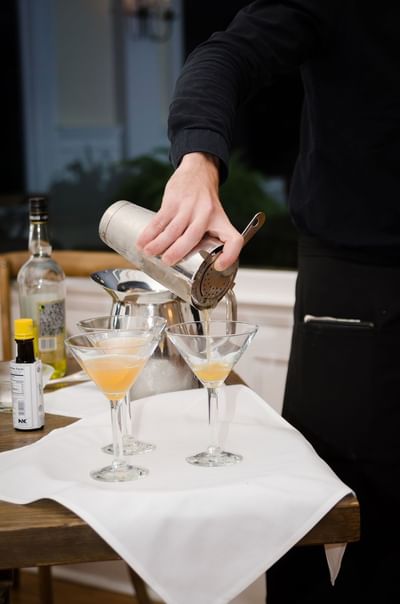 Bartender pouring a orange colored cocktail into glasses from a mixture at The Stanley Hotel