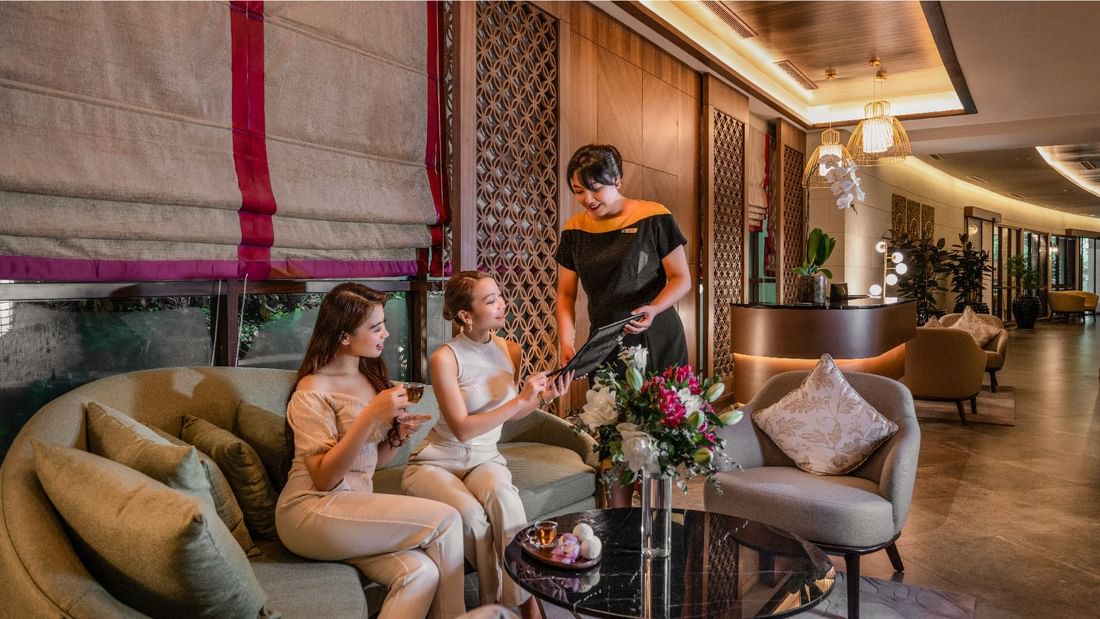 A waitress showing a menu to two women sitting on a sofa at the Sunway Resort
