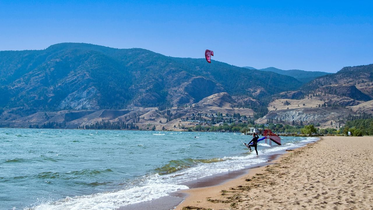 A person surfing on a lake with mountains in the background under a clear sky.