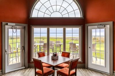 Indoor dining table by a large arched window with a scenic golf course view at Rodd Crowbush Golf & Beach Resort