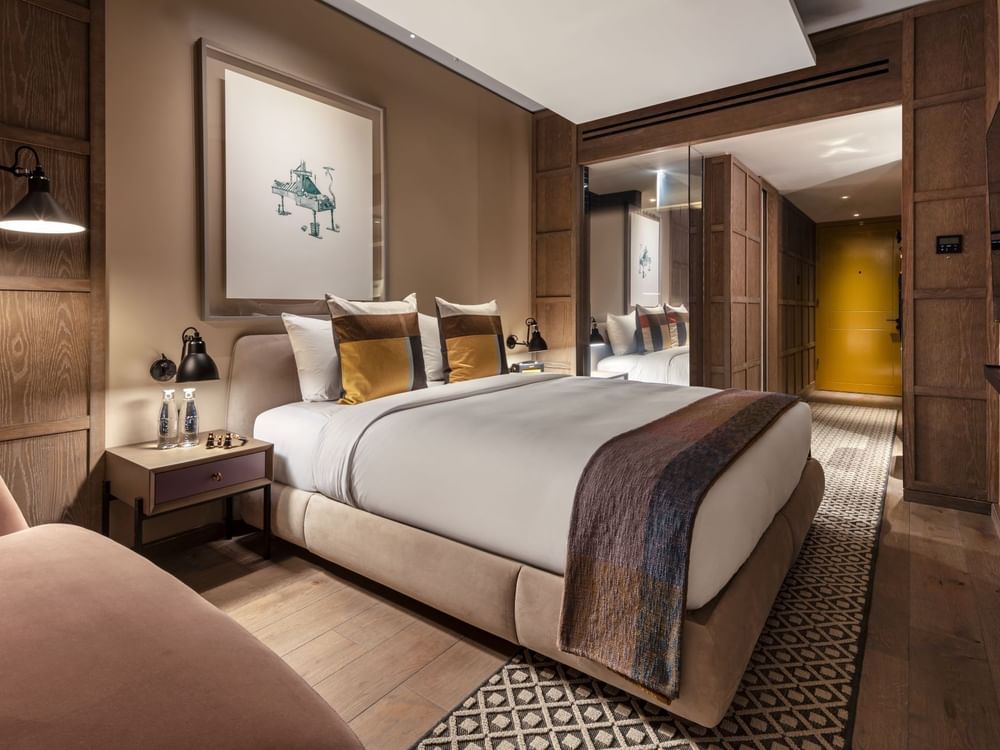 Bed with a side table and hanging wall art in Deluxe King Room at The Londoner Hotel