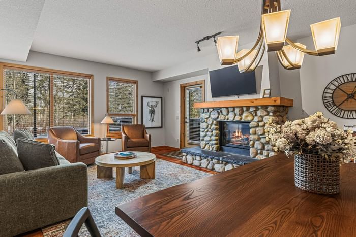 Cozy living room with a fireplace, modern chandelier and forest view at Spring Creek Village Canmore