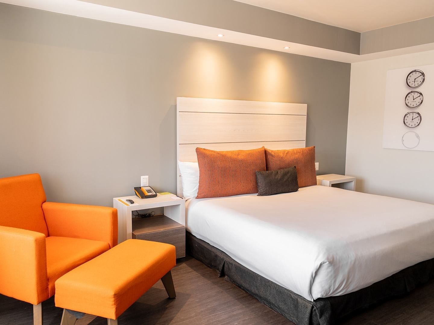 Nightstands and cozy lounge  chair by the bed in the King Executive Room with wooden floors at the Real Inn Tijuana