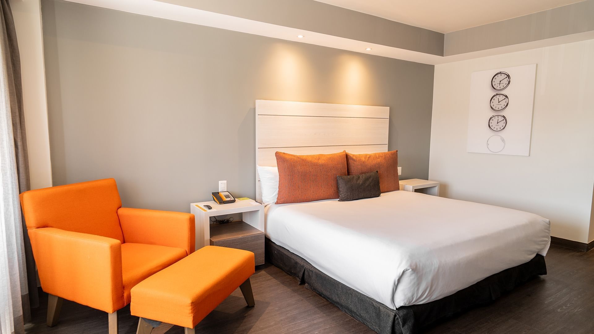 Nightstands and cozy lounge  chair by the bed in the King Executive Room with wooden floors at the Real Inn Tijuana