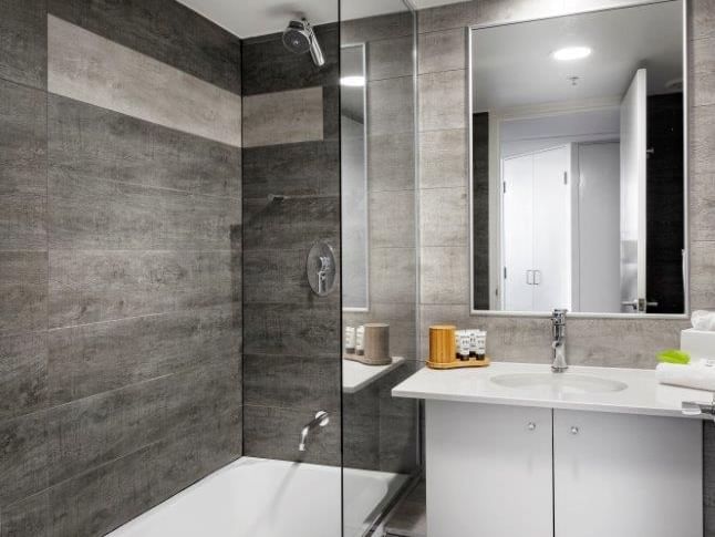 Studio Room bathroom with grey wood-look tiles, a white vanity, and a glass-enclosed shower at The Sebel Brisbane
