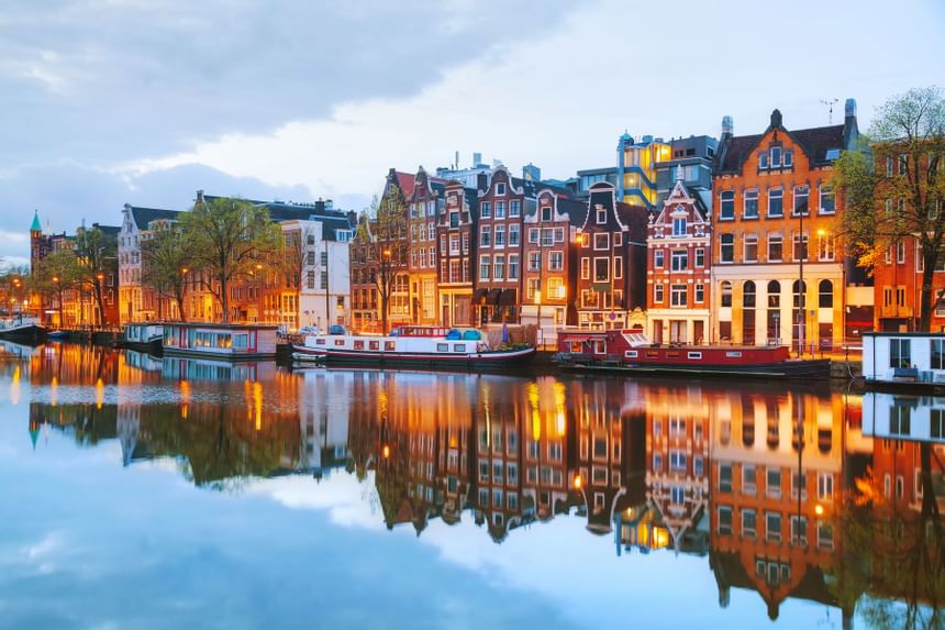 A serene canal with boats docked along a row of historic buildings, reflecting in the water at dusk.