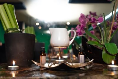 Velas y macetas de plantas en una mesa con una tetera sobre un soporte de velas.