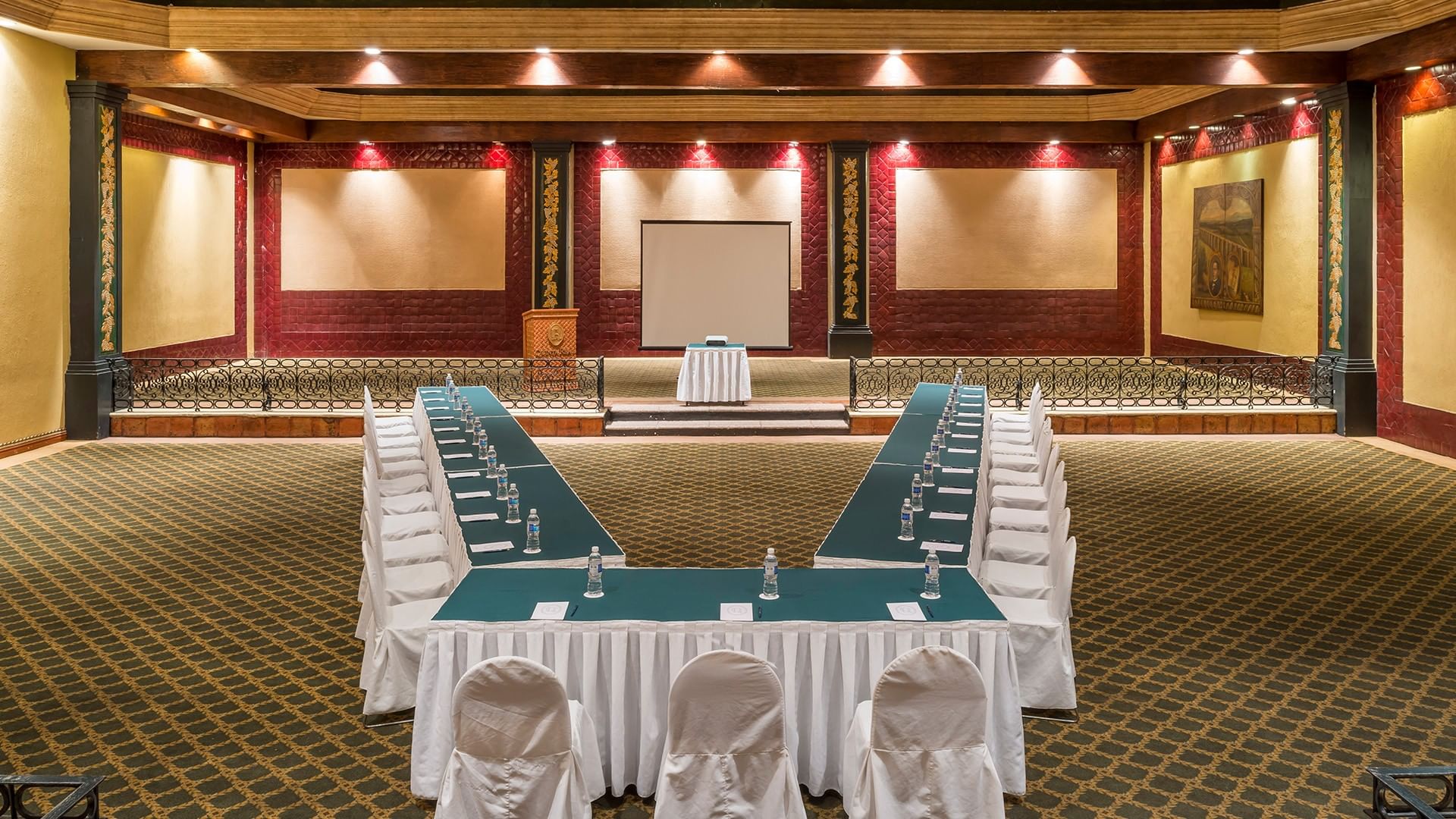 Large Salón San Marcos featuring a podium, projector screen, and patterned rug at Quinta Real Aguascalientes