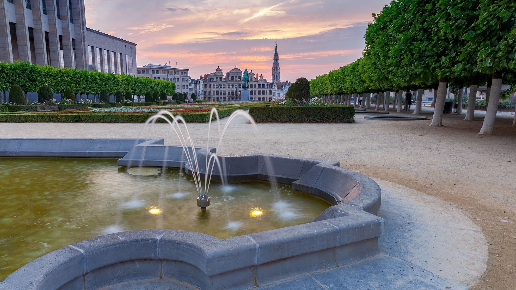 A scenic park near Warwick Hotels and Resorts featuring a fountain, manicured hedges, and historic buildings in Brussels