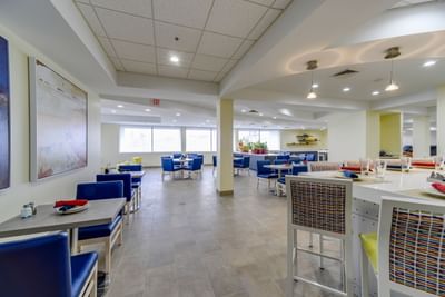 Lounge area with TV, blue chairs and tables arranged at St. Louis Airport Hotel
