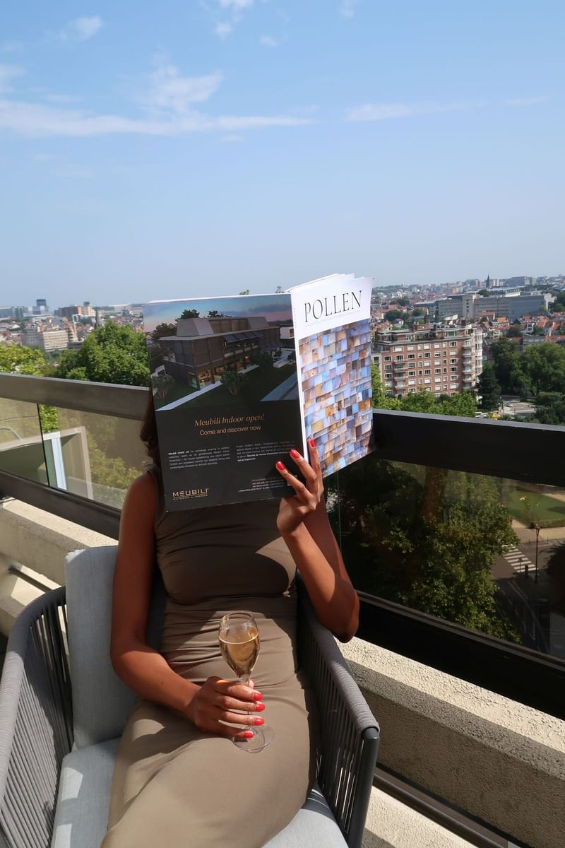 Guest reading a magazine while enjoying white wine on a terrace overlooking Brussels at Hotel Barsey by Warwick Brussels Bruxelles
