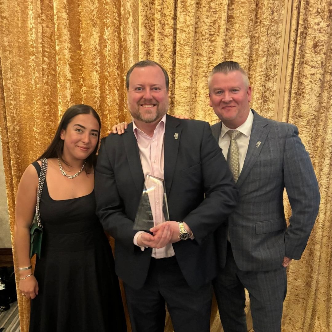 Three people holding a Hospitality Award with a gold curtain backdrop at Hotel Brookmere & Arbor Spa