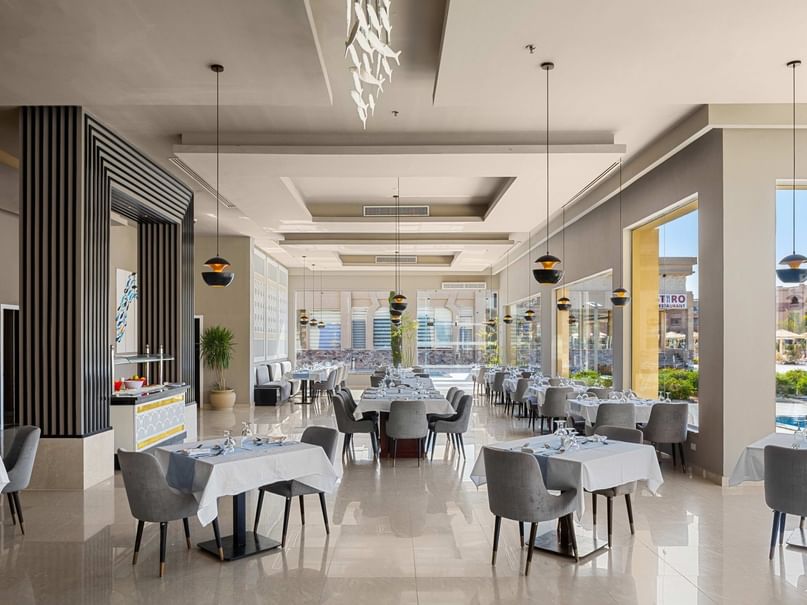 Elegantes Restaurant mit weißen Tischen, Stühlen, großen Fenstern und Blick auf den Pool.