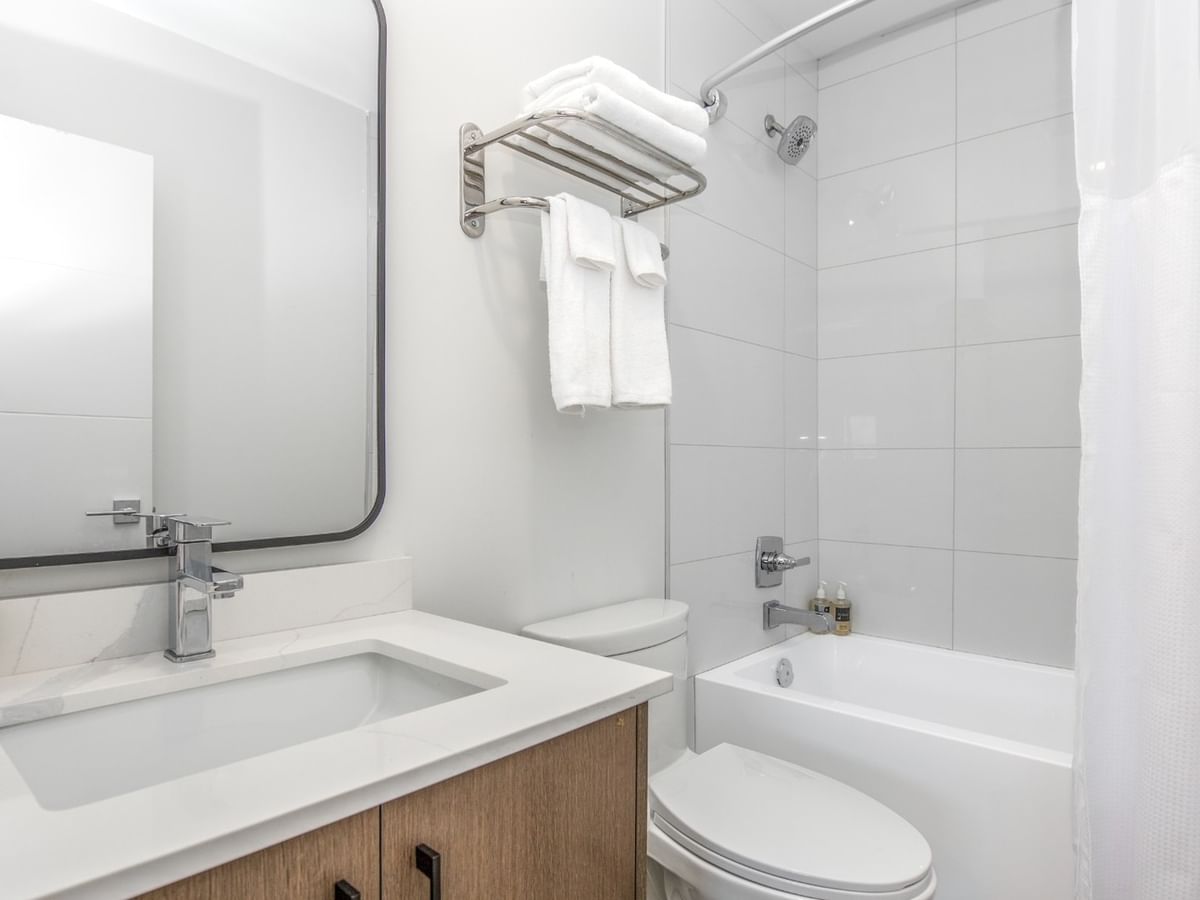 Modern white bathroom with a toilet, sink, mirror, white bathtub, and towels.