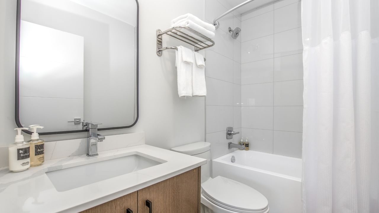 Modern white bathroom with a toilet, sink, mirror, white bathtub, and towels.