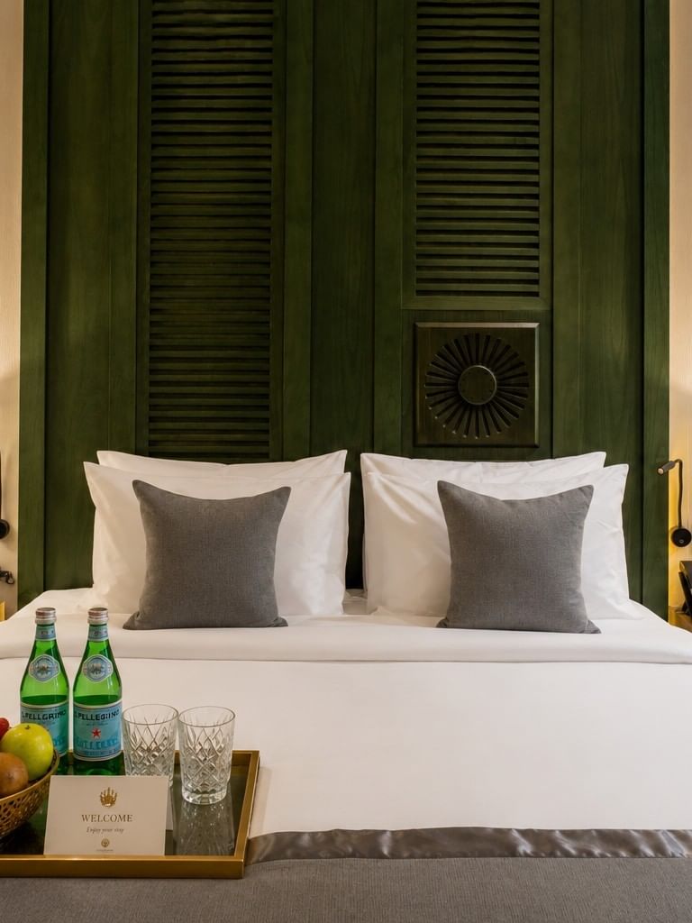 Fresh fruit basket with bottled water on bed before dark paneled headboard in Accessible Room at Naviti by Warwick Jeddah