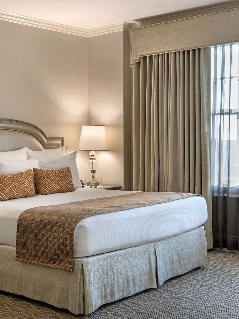 King bed with a patterned throw by bedside lamps under a valence in Classic King Accessible at Warwick Melrose Dallas