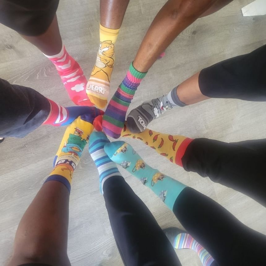 Group of people standing in a circle showcasing colorful character socks with patterns by each other at Time Out Hotel