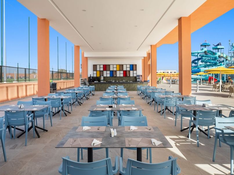 Tables and chairs set up in a restaurant with a colorful wall and waterpark in the background.
