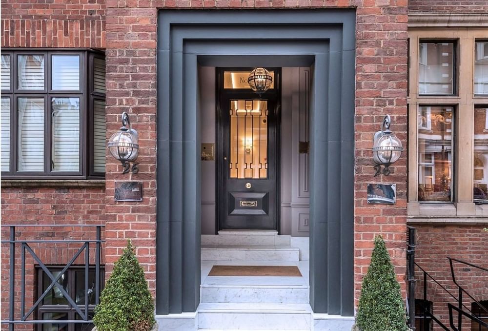 Grand entrance with topiary by a black door, framed in stone brick at The Capital Hotel, Apartments and Townhouse
