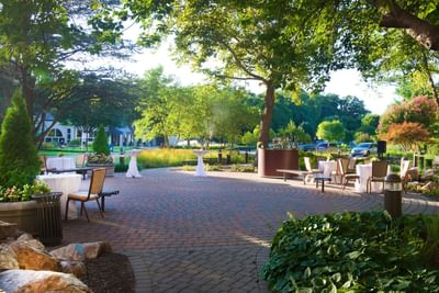 The patio at the Bolger Center features a stone-paved area with tables and chairs under lush green trees