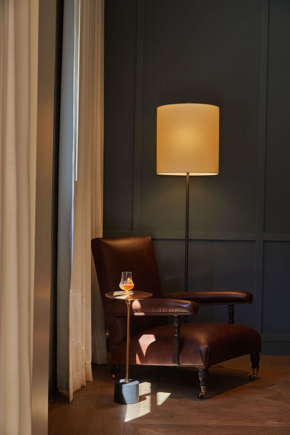 Cozy corner featuring a leather armchair, a side table with a drink, and a warm floor lamp at El Prado Hotel