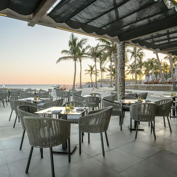 Outdoor dining terrace in Pergola at Marquis Los Cabos Resort overlooking the ocean with stylish tables and chairs at sunset