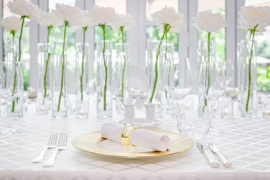 Table with a gold plate, white napkin, and tall glass vases of white flowers at Park Hyatt Saigon