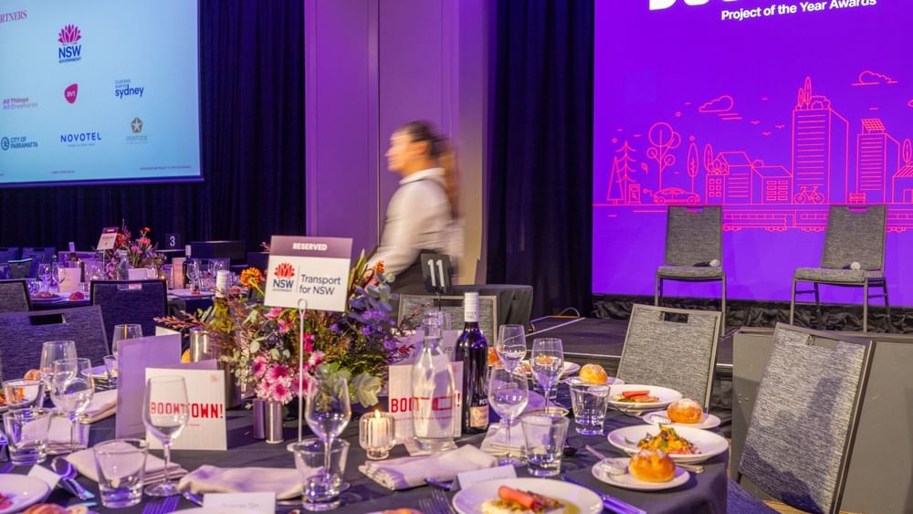 Set a banquet table with a floral centerpiece and wine near the stage in the Freshwater Room at Novotel Sydney Olympic Park