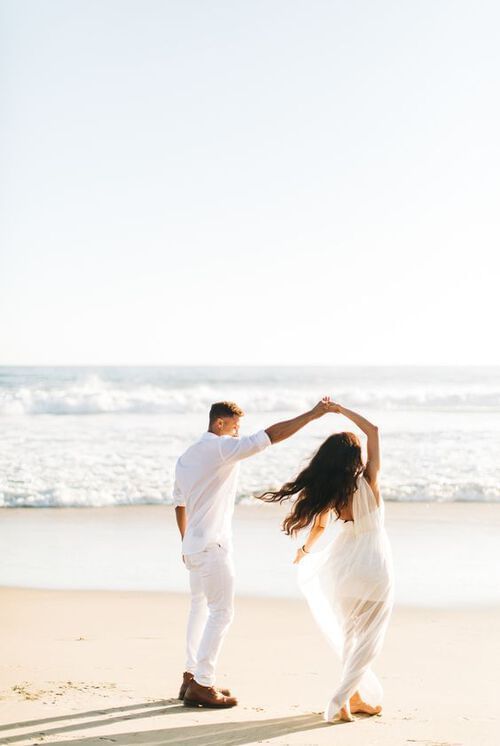 A couple joyfully dancing together on a beach with the ocean waves near Grand Park Kodhipparu, Maldives