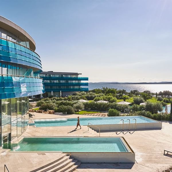 Eine Person läuft am Rande eines modernen, blauen Pools mit Blick auf das Meer vorbei.