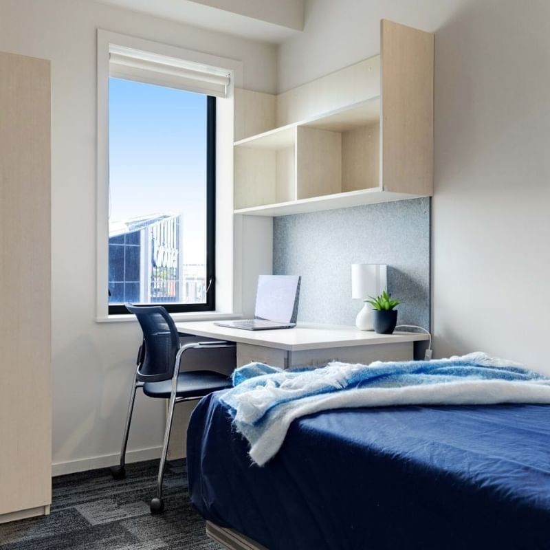 Neat bedroom with bed, desk, chair, and window at UniLodge Wellesley Apartments.