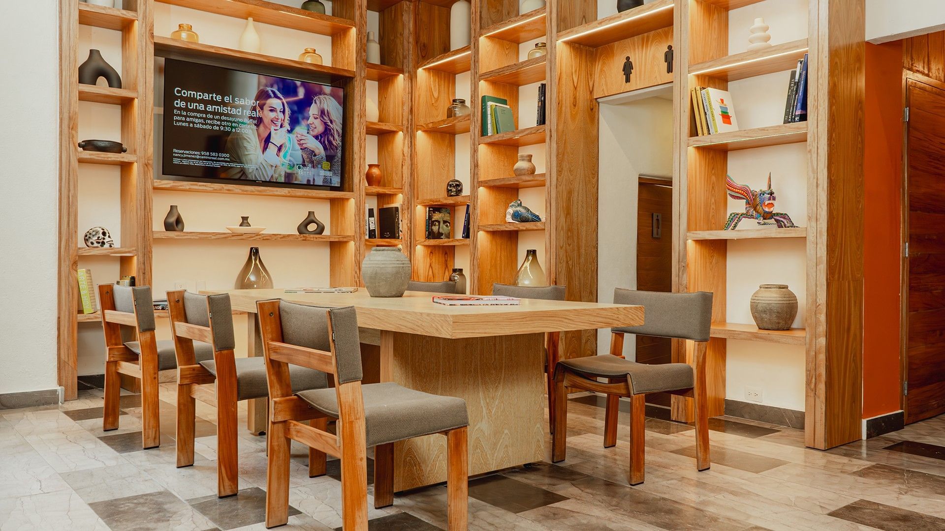 Dining table with cozy chairs, wall-mounted TV, and backlit shelves in Library Café & Deli at Camino Real Zaashila Huatulco