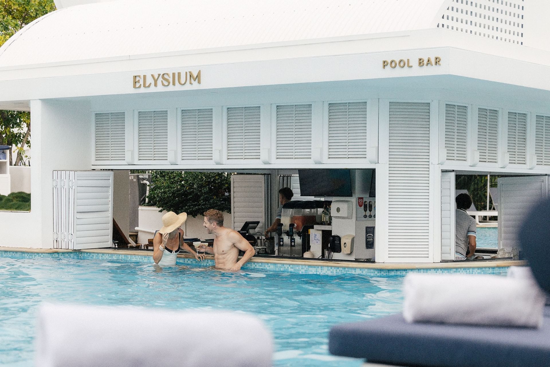 Outdoor pool bar at Elysium Hotels showing a smiling couple in swimsuit enjoying refreshing drinks at swim-up counter