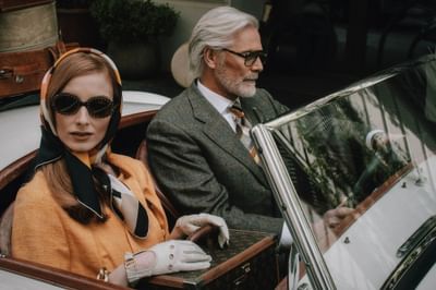 Stylish couple in elegant attire sitting in a vintage convertible, luggage in the background at Hotel Motto Vienna